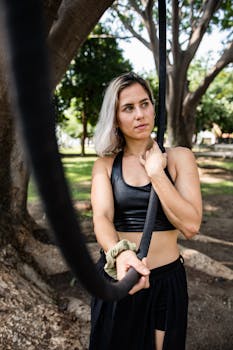 Fit woman exercising with a rope outdoors in a park setting, showcasing strength and focus.