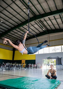 A woman performs aerial acrobatics on a hoop in a spacious gym, showcasing strength and flexibility.