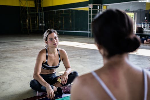 Two women in a workout session, sitting on the gym floor, focused and relaxed.