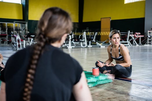 Two women in a gym, one with braided hair, engaging in a fitness session with equipment.