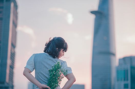 日落时分，一名女子身穿时尚服装，手持鲜花，俯瞰着现代城市的天际线