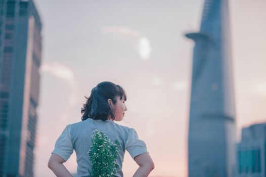 日落时分，一位手持鲜花的女子融入城市景观，将自然与现代建筑融为一体