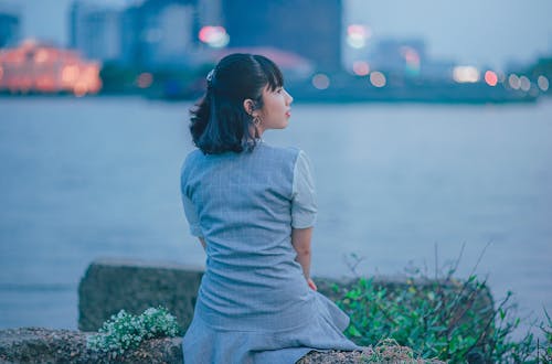 Free Woman Wearing Gray Dress Sitting Near Body of Water Stock Photo