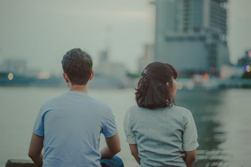 Free A serene moment of a young couple sitting by the river, enjoying the cityscape at dusk. Stock Photo