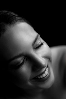 Elegant black and white portrait featuring a young woman smiling with eyes closed, creating a serene and timeless feel.