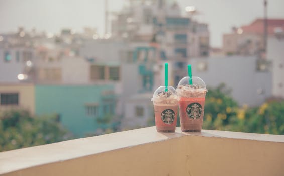 Two Starbucks iced drinks on a sunny balcony with a cityscape background.