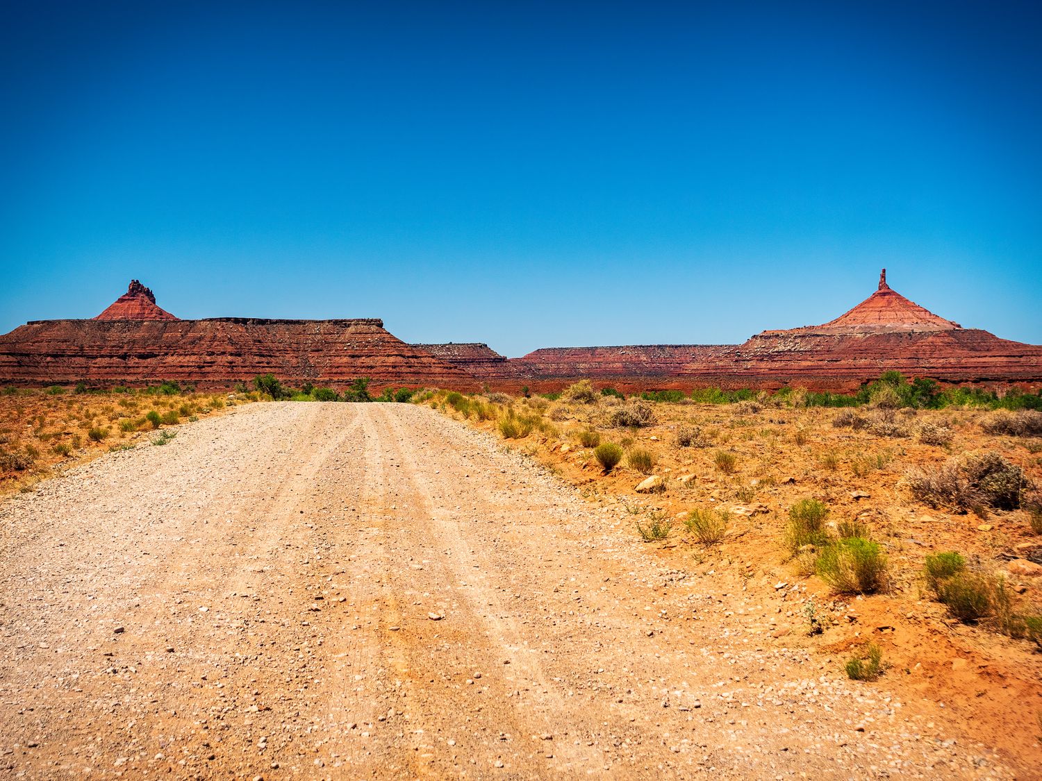 Dirt overlanding road leading toward iconic Utah red sandstone buttes under a deep blue desert sky