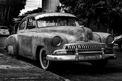 Free A vintage car is parked on a street, showcasing its rusted charm in a black and white photograph. Stock Photo