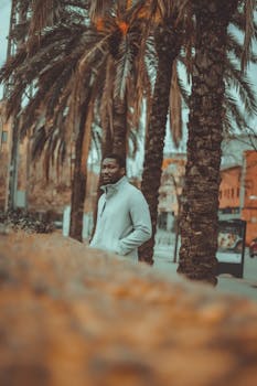 African American man in a jacket walking through a palm-lined street on a moody day.