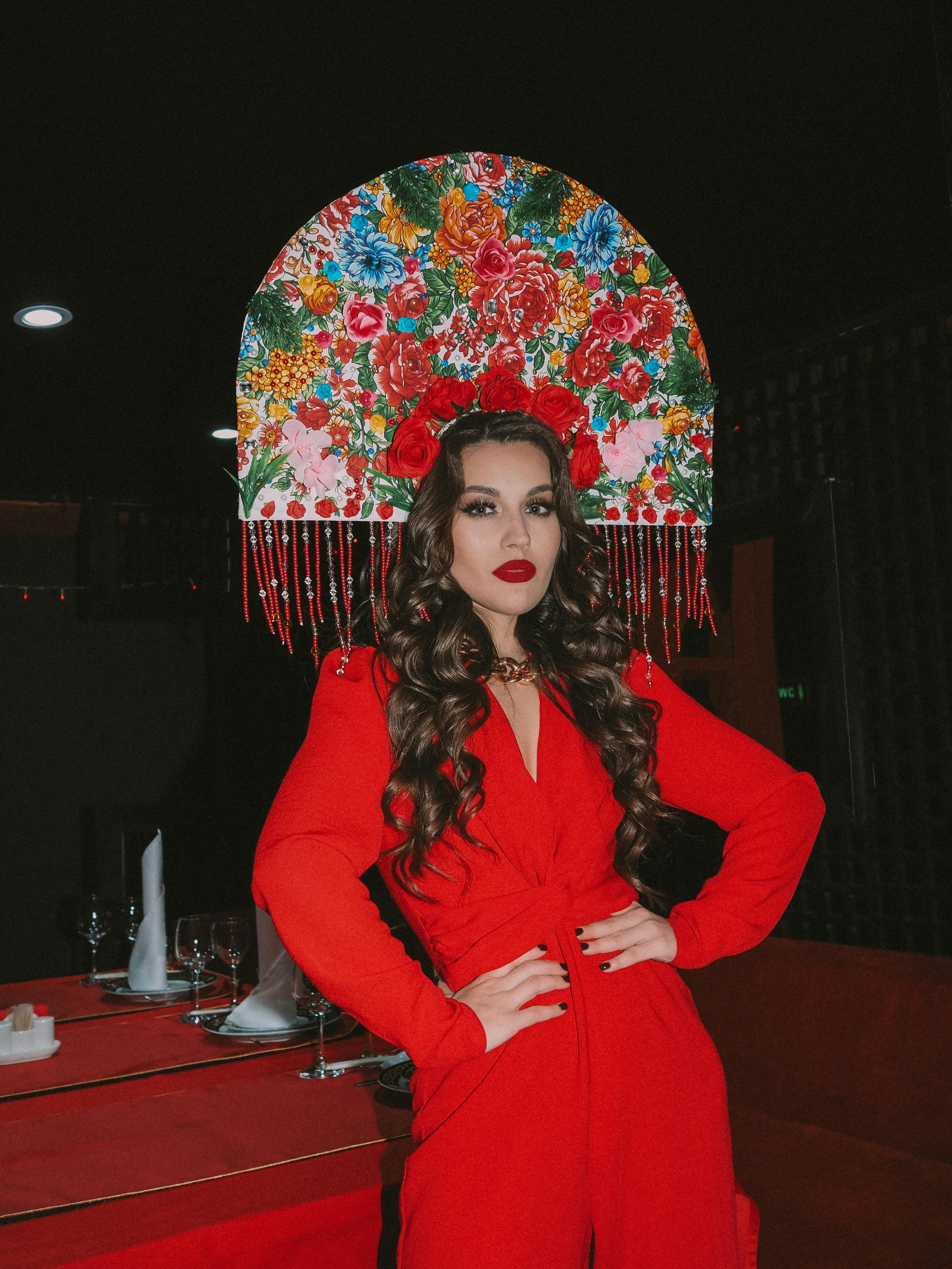 Stylish woman in red dress and floral headdress posing indoors with confident gaze.