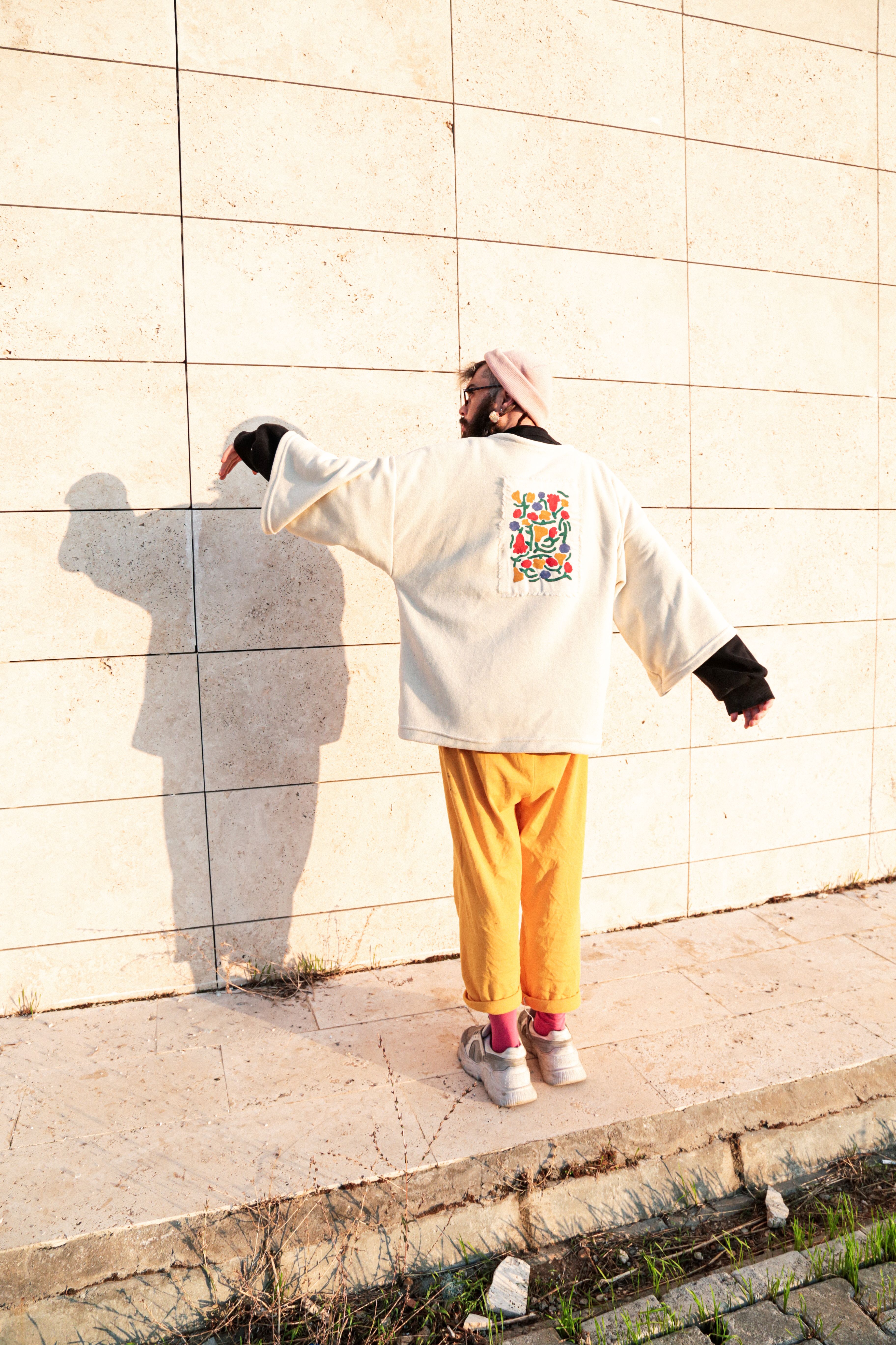 A person in a vibrant outfit stands against a wall casting a shadow.