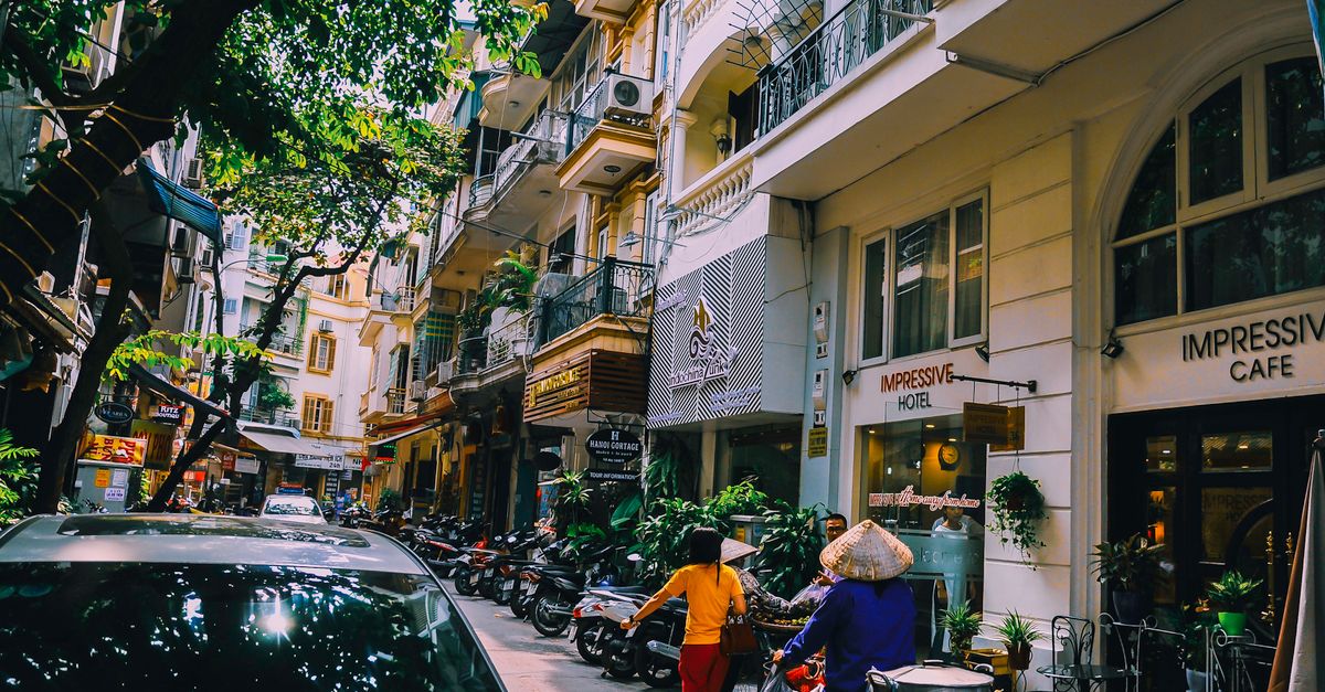 Vibrant street life in Hanoi with locals, cafes, and motorbikes on a sunny day.