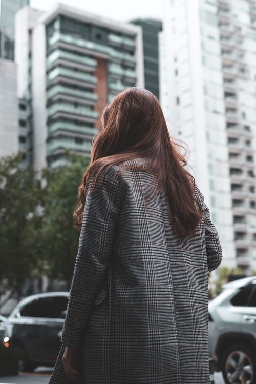 Free A woman in a checkered coat stands in a bustling city with tall skyscrapers. Stock Photo