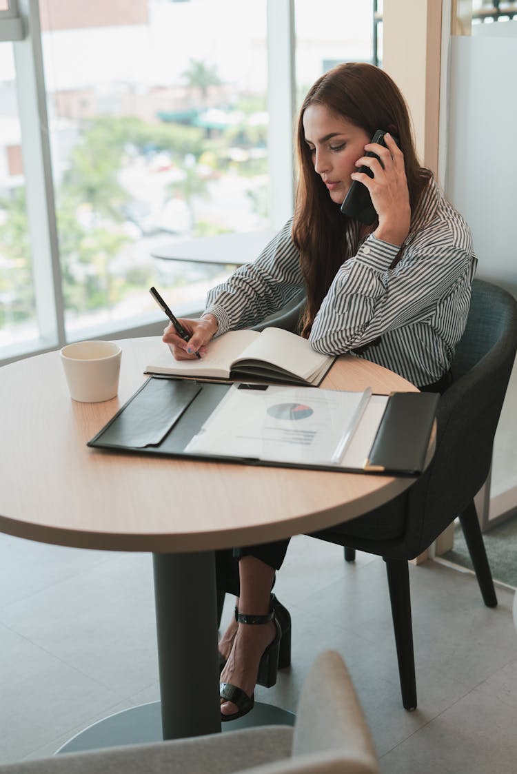 Sitting Woman Talking On Phone And Writing In Notebook