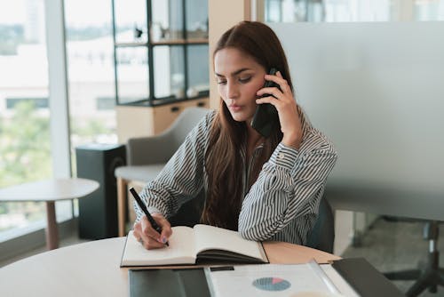 Free Businesswoman Talking on Phone and Taking Notes Stock Photo