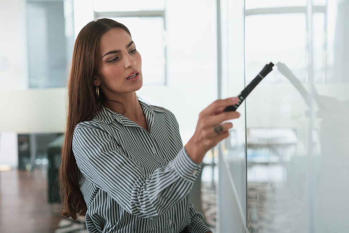 A Latina businesswoman writing on a whiteboard during a presentation — Paloma, for BossBabe Gangster (bossbabegangster.com)