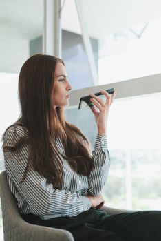 Young businesswoman using voice assistant on her phone in a modern office setting.