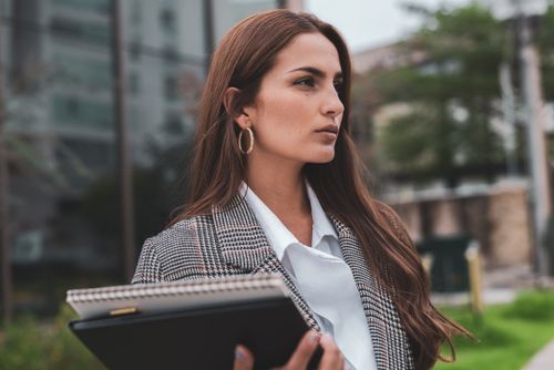 Free Portrait of a confident businesswoman outdoors in formal attire, holding a notebook and exuding professionalism. Stock Photo