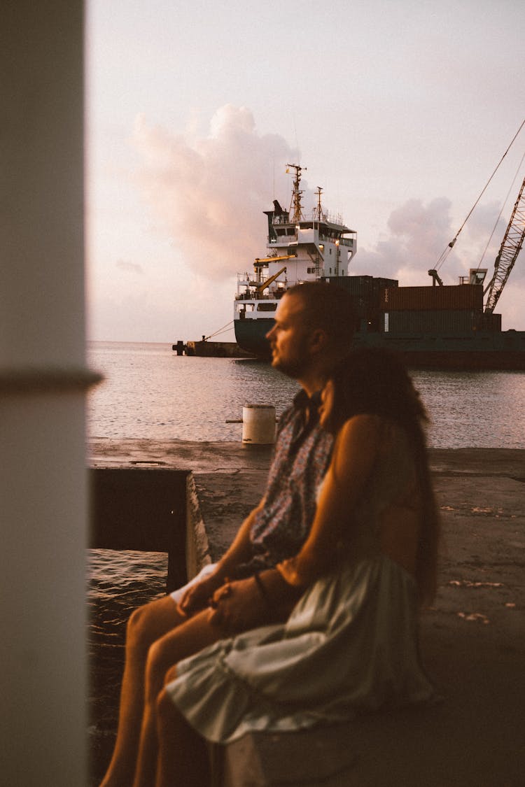 A Couple Sitting On The Edge Of The Port