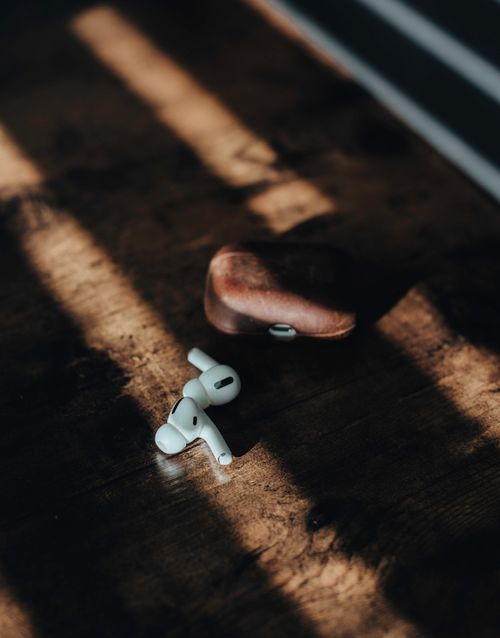 Free Close-up of wireless earbuds and brown case casting shadows on wooden surface. Stock Photo