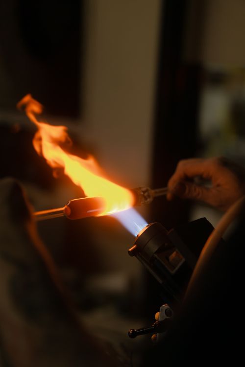 Free Close-up of artisan glassblowing with a torch and intense flame. Captures heat and creativity. Stock Photo