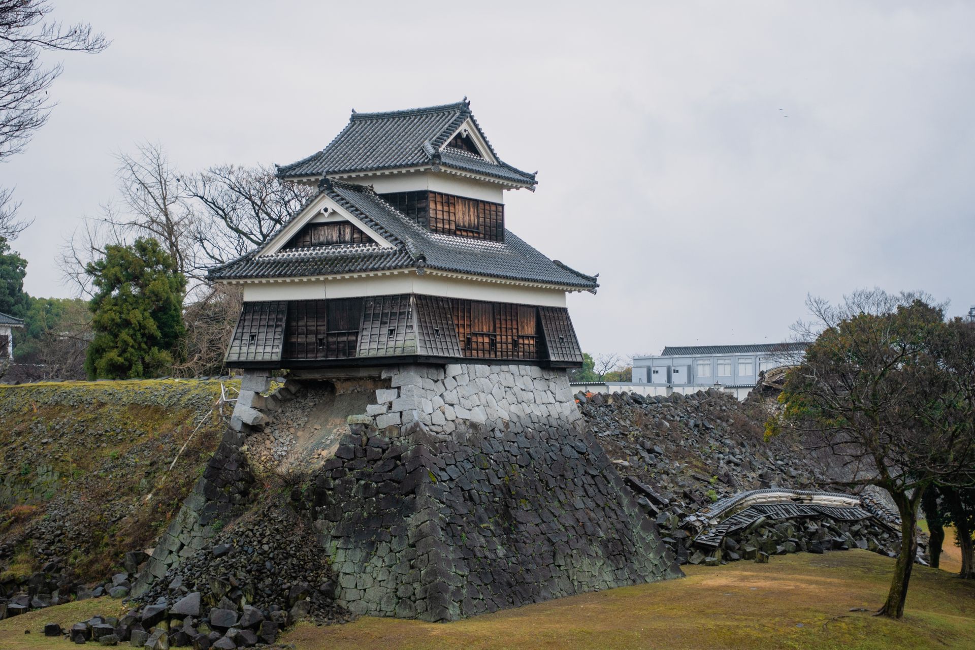 A damaged battlement of Kumamoto Castle amid a landscape of rubble and greenery.