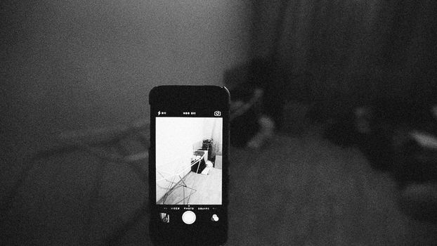 Artistic grainy black and white image of a smartphone capturing a room scene.