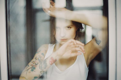 Free Woman Wearing a Tank Top Leaning on a Glass Window Stock Photo