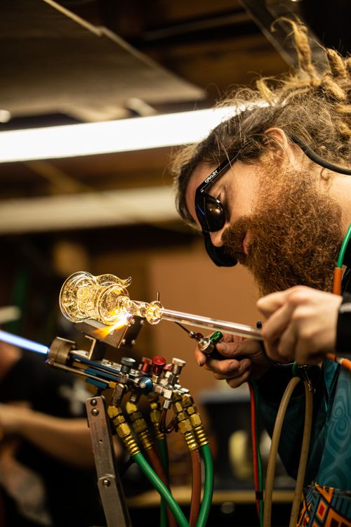 Free A skilled glassblower creating an intricate piece in a workshop, focused and wearing protective eyewear. Stock Photo