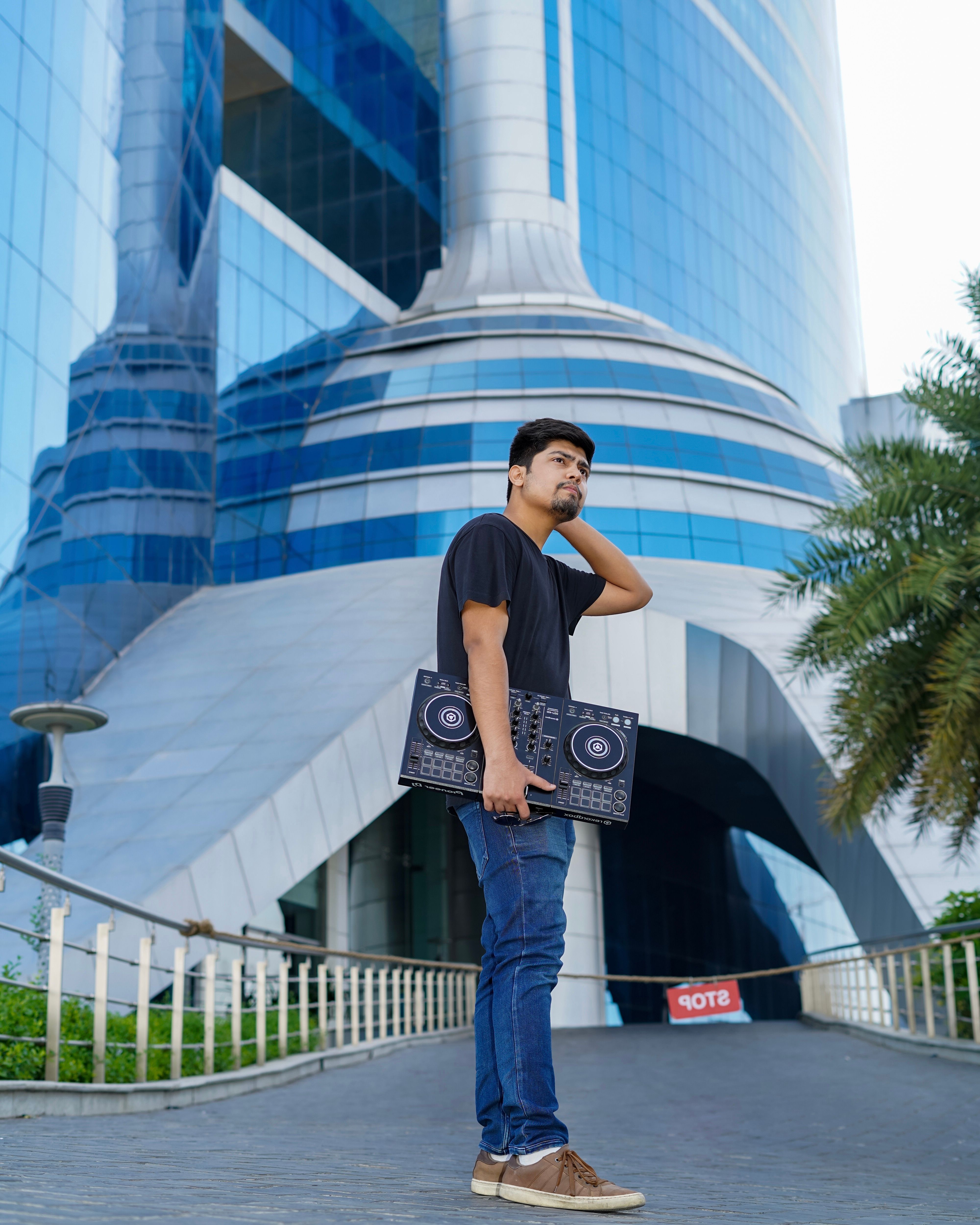 Man holding a DJ turntable stands in front of a futuristic skyscraper.