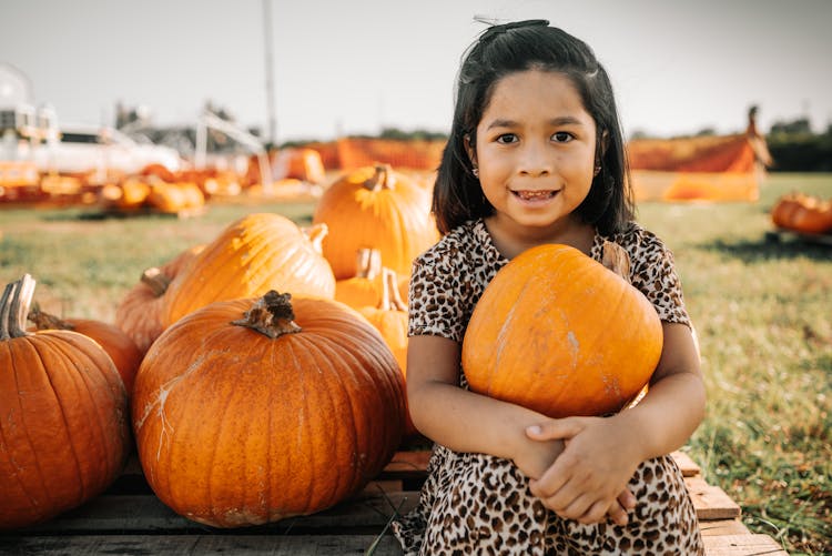 A Girl In Leopard Print Dress Holding A Pumpkin