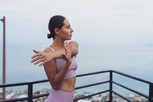 Free A young woman in workout attire stretching on a balcony with a sea view. Stock Photo