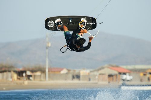 Free A thrilling kiteboarder performs a midair trick against a scenic beach backdrop. Stock Photo