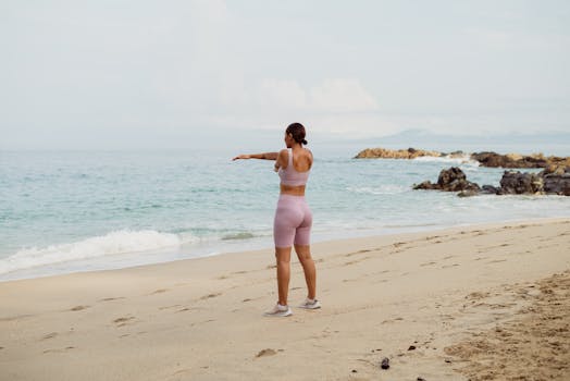 Woman in activewear stretching on a serene beach setting with ocean waves.
