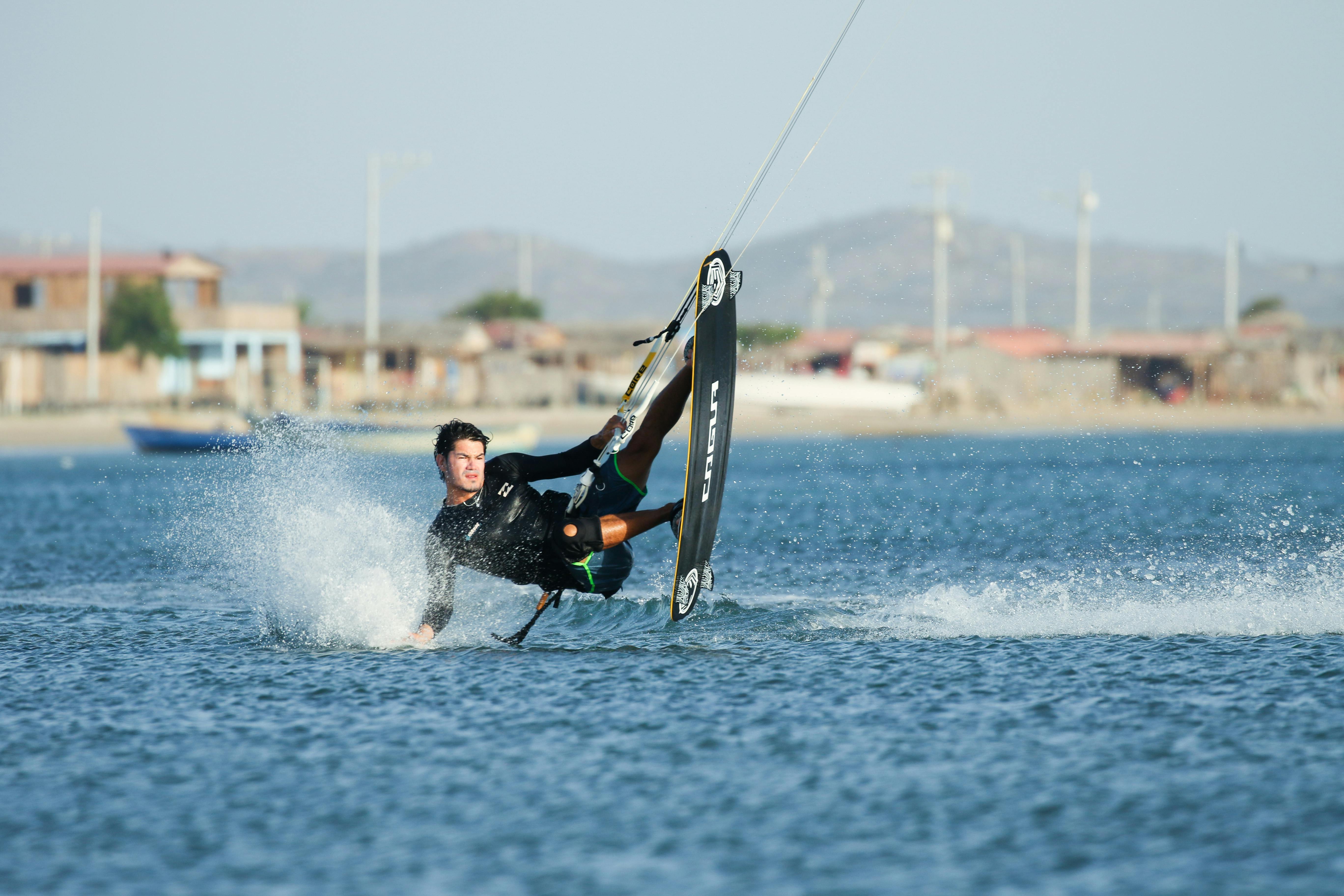 Man performing a thrilling kitesurfing stunt on the water near a beach on a sunny day.