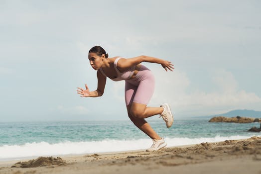 A woman in sportswear running on a sunny beach, showcasing fitness and determination.