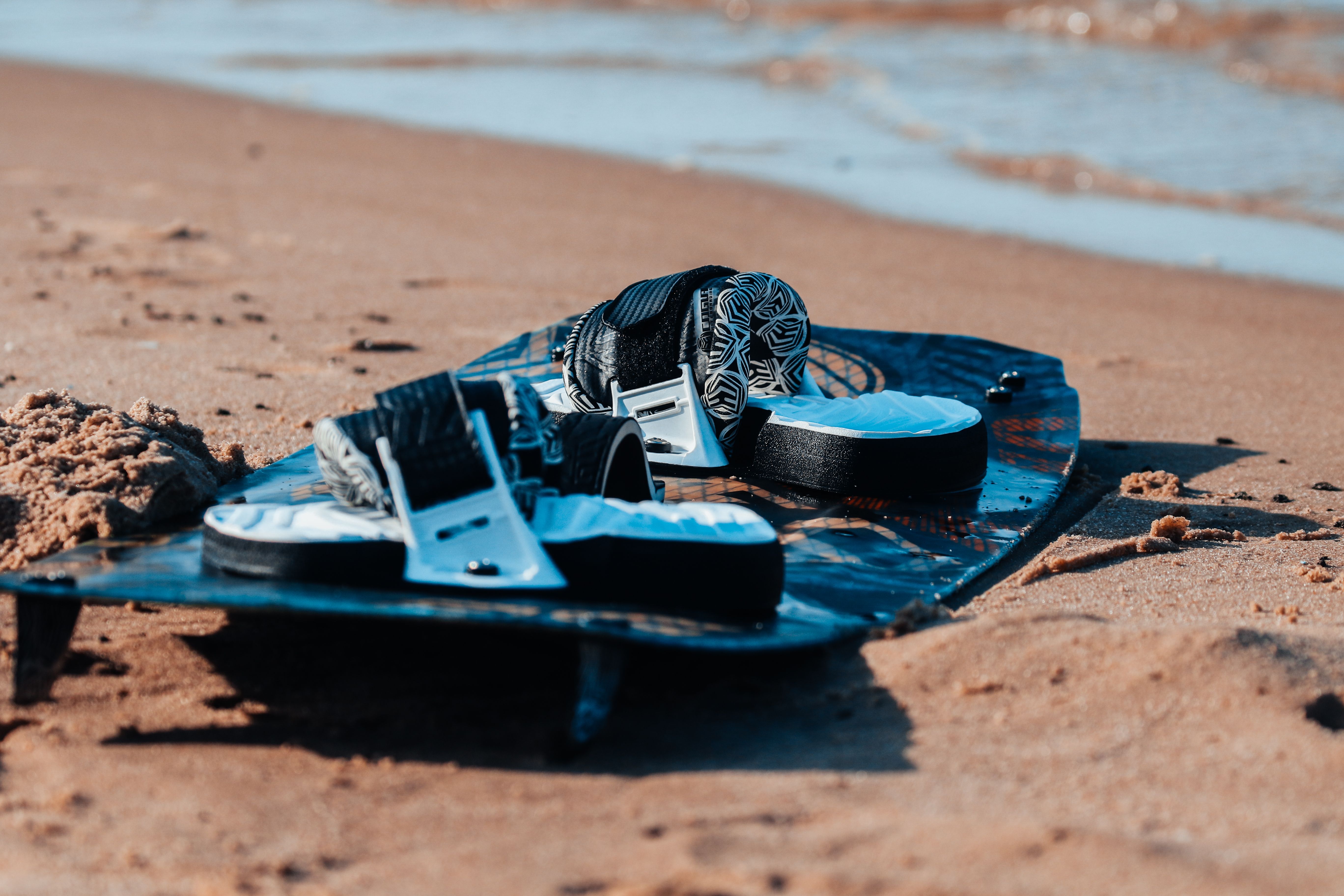 Prancha de surf e botas na areia da praia, simbolizando lazer e esportes aquáticos.