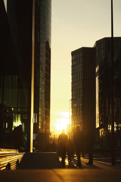 Free Silhouetted people walking among skyscrapers in Moscow at sunset, creating a warm twilight scene. Stock Photo