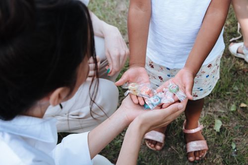 Free A child shares colorful wrapped candies with an adult in a park setting. Stock Photo