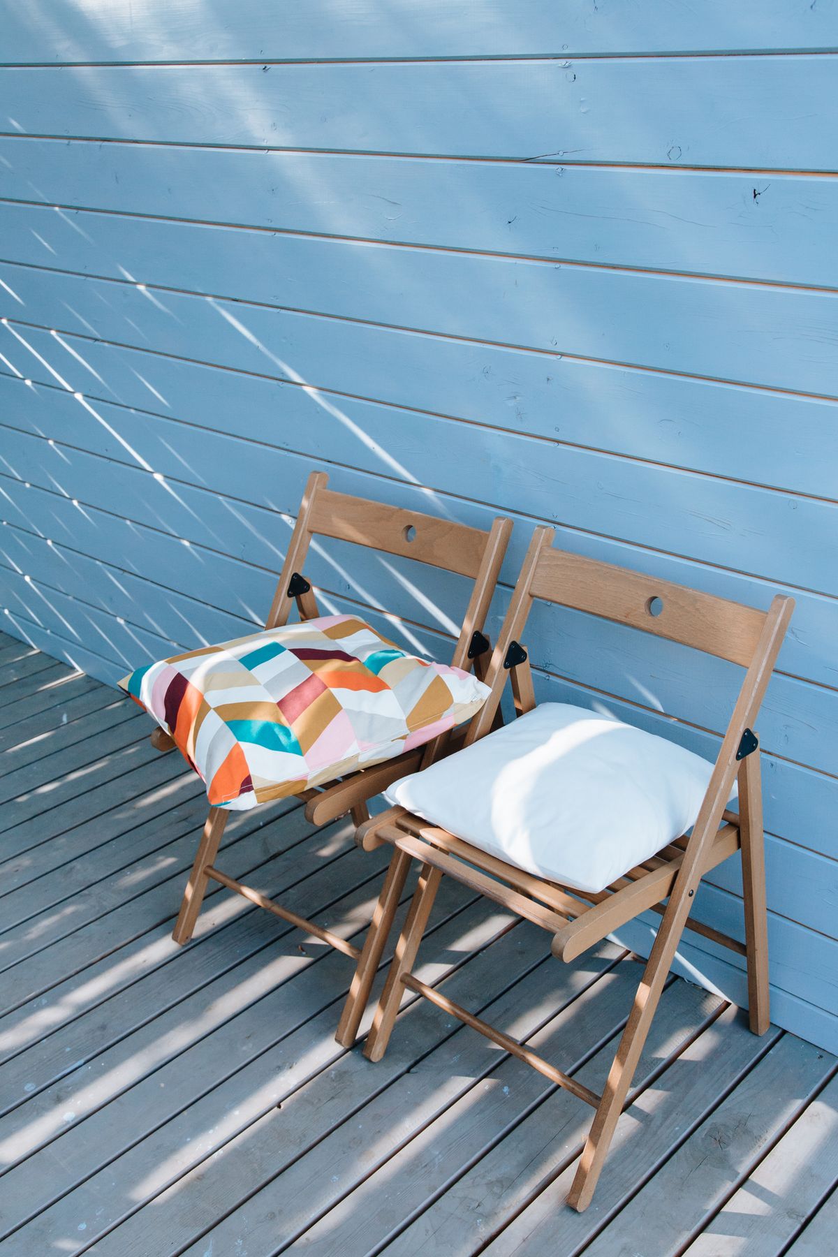 Pair of foldable wooden chairs with cushions on a sunny blue porch. Perfect for outdoor relaxation. Stock Photo.