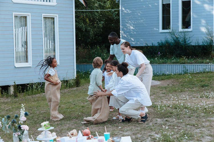 Children Playing Sack Race Outside The House With Their Family