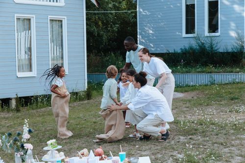 Free Joyful family gathering with children playing sack race in a garden outside a house. Stock Photo
