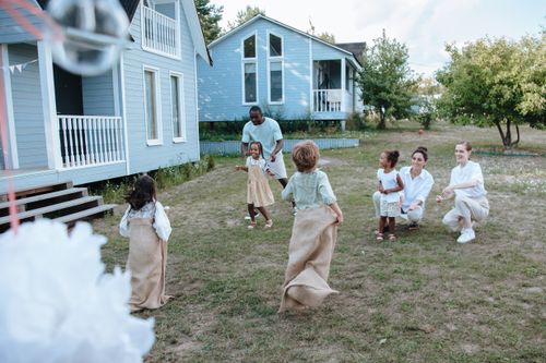 Free Children and adults have fun with a lively sack race outside a cozy home on a sunny day. Stock Photo