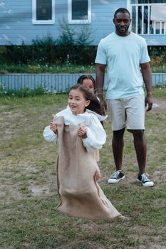 A young girl enjoys a sack race outdoors while a family member watches with joy.