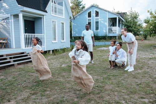 Free Group of children enjoying a sack race in a backyard setting, surrounded by family. Stock Photo
