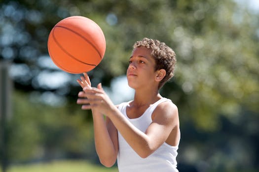 A young boy in a white tank top focuses on a basketball outdoors on a sunny day.