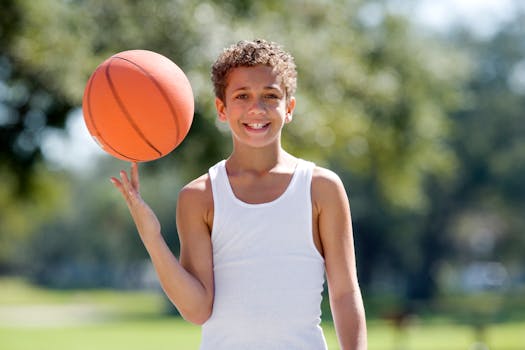 Smiling boy spinning basketball on finger in a sunny outdoor park.