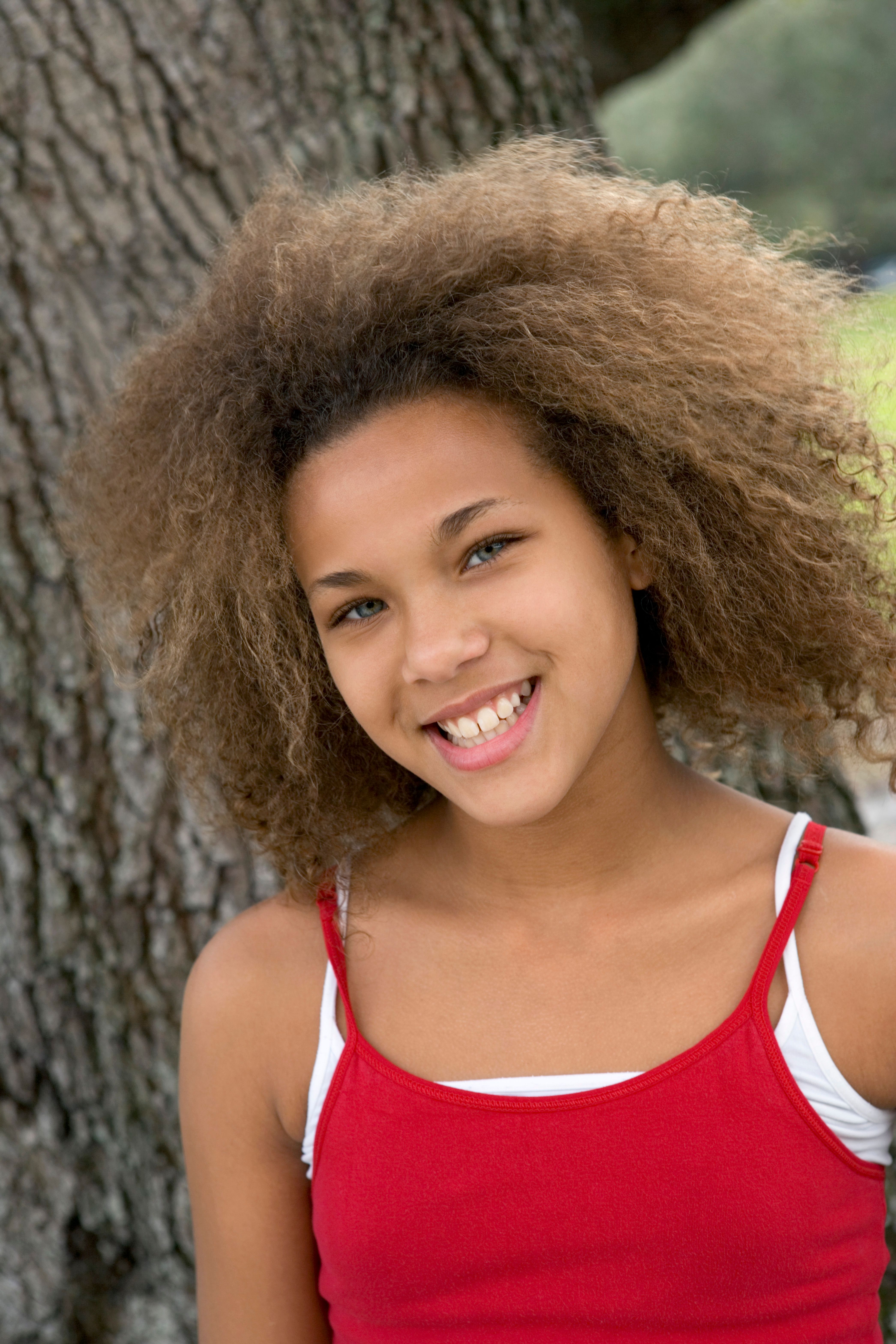 Portrait of a happy teenage girl with afro hair wearing a red top, smiling outdoors.