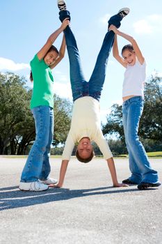 Three children enjoy a sunny day performing a playful handstand outdoors.