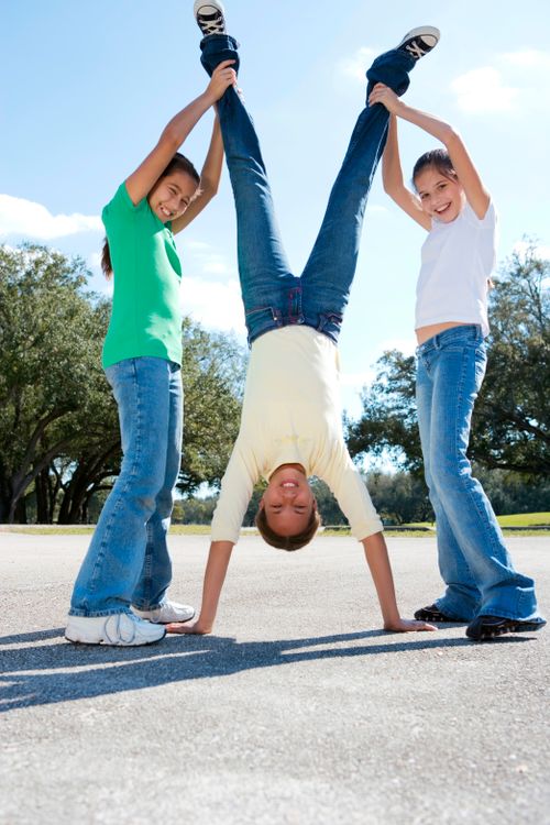 Free Three children enjoy a sunny day performing a playful handstand outdoors. Stock Photo